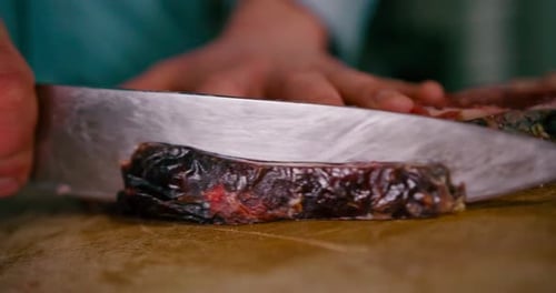 Close up view of chef hand slicing the steak with Steel knife on a wooden chop board.