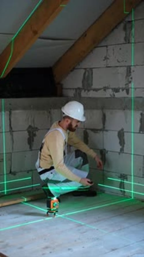 Construction worker installing and adjusting laser level on floor before measuring