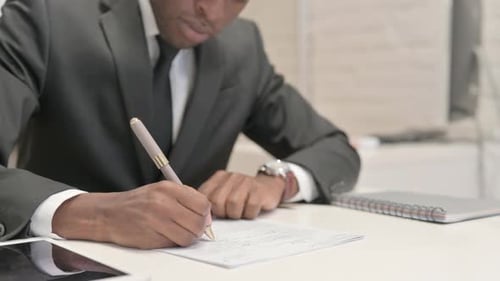 Close Up of African Businessman Writing Documents