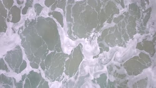 Stürmisches Meer mit brechenden Wellen, weißem Schaum und Strandsand ins Meer gezogen