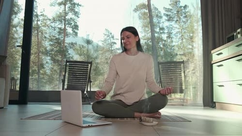 Woman Practicing Online Yoga Meditation with Laptop in Modern Apartment