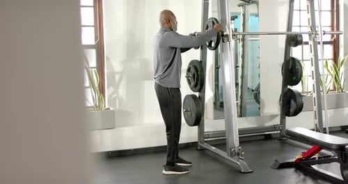 Afroamerikaner nähert sich der Smith-Maschine, lädt Hantelscheiben vom Gestell und bereitet das Training vor