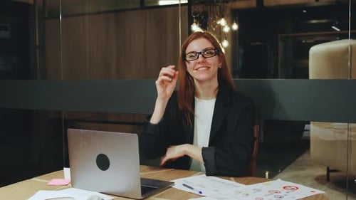 In a Bright Office a Confident Young Woman in Stylish Glasses Smiles at the Camera While Working on
