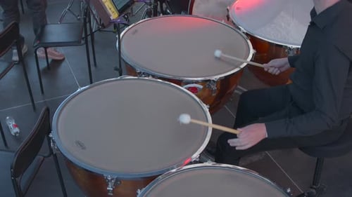 Close View Of Timpani Player Adjusting Pitch Amidst Orchestral Rehearsal With Dramatic Lighting