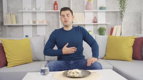 Man Sitting on Couch Eating Meal and Drinking Water