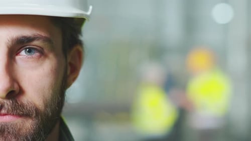Close Up of Half Face of Man Engineer in White Helmet Looking Straight to Camera Inside Manufactory