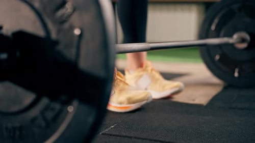 Closeup in the Gym Girl Trainer in Black Leggings is Going to Lift a Barbell with a Weight