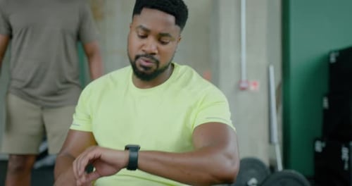 Male Checking Results on Smart Watch in Gym on Rowing Machine