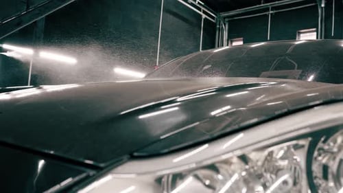 close-up A male car wash employee applies car wash detergent to a black luxury car using spray gun