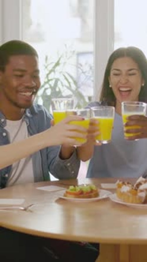Happy Multiethnic Friends Toasting with Juice During Breakfast at Home