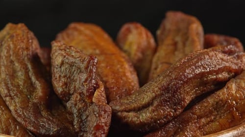 Small dried bananas spinning on black background close up. Sweet dried fruits made from dehydrated