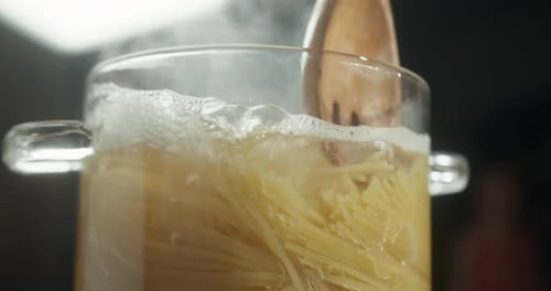 Pasta is Cooking in a Glass Pot Steam Rising Above Cook Stirs with a Wooden Spatula Hot Water Boils