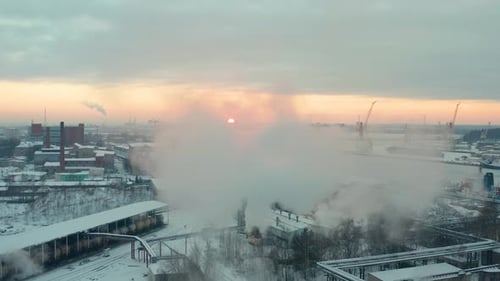 Fly over aerial view of industrial port in winter, covered with show. Low sun at sunset. Moving forw