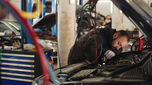Car mechanic at a car service station repairs a car under the car hood and check up the engine