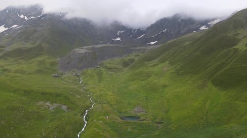 drone shot of lake and river in the middle of mountains with cloud and fog in the background