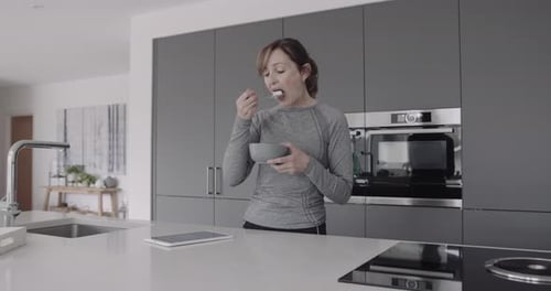 Woman Eating Cereal and Using a Tablet