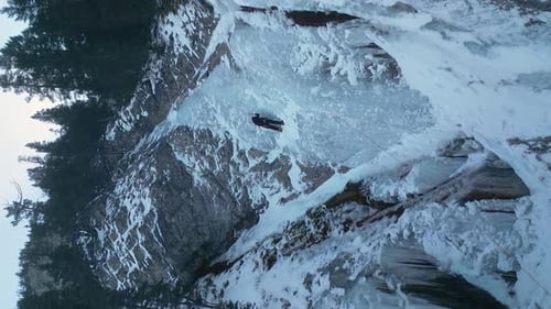 Vertical format Ice climber climbs steep frozen waterfall on mtn cliff