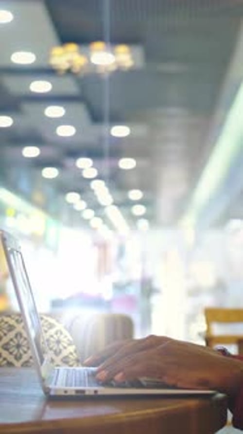 Person Using Laptop at a Cafe Table with Blurred Background and Warm Ambient Lighting