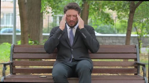 Mature Adult Businessman Experiencing a Headache in the Park