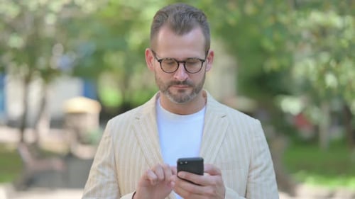 Man with Mobile Phone Reading Outdoors in Suit