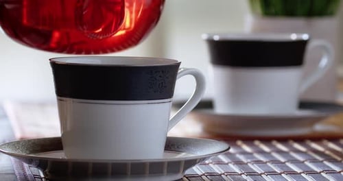 Teekanne gießt Tee in eine Tasse
