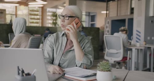 Ambitious Business Lady Speaking on Mobile Phone and Reading Papers Working in Open Space Office