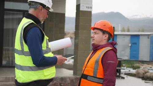 Two workers engineers use paper blueprint and discuss work. Specialist talks to technician