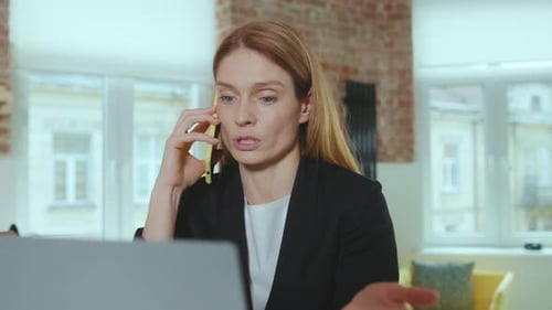 Close Up Serious Young Businesswoman Speaking on Smartphone Use Laptop Computer at Home Office