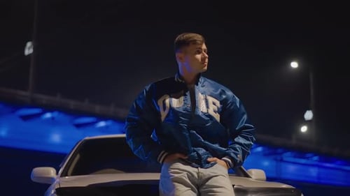 Urban Scene Featuring Man with Vapor Beneath Bright Streetlights Stylish Male Posing on Vehicle Hood