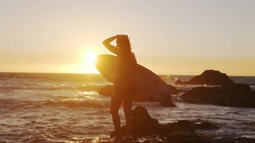 Surfer with Surfboard at Sunset on Rocky Beach
