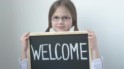 Little School Girl in Glasses Holding Welcome Inscription on Chalkboard