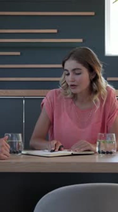 Vidéo verticale : Femme ajustant ses cheveux et parlant à un collègue tout en notant dans un carnet