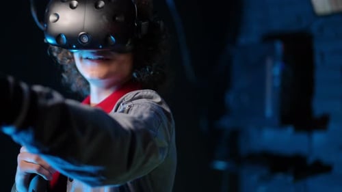 Closeup A Teenager Wearing VR Glasses and Holding Controllers in His Hands Moves Through a Dark Room