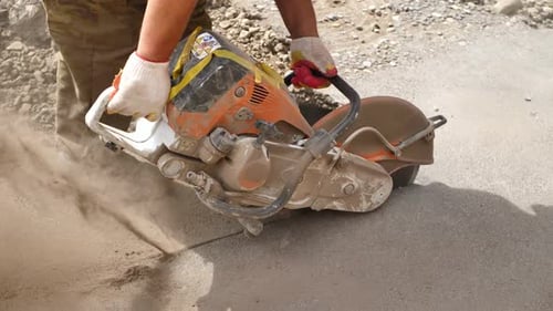 A Road Builder in Uniform Cuts Off the Old Asphalt with a Hand Grinder According to the Markings