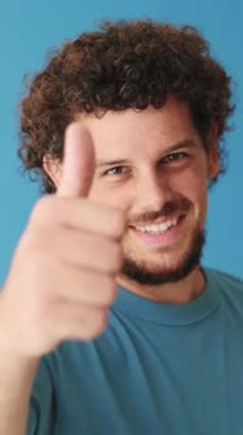 Close up, happy man showing thumbs up gesture isolated on blue background in studio