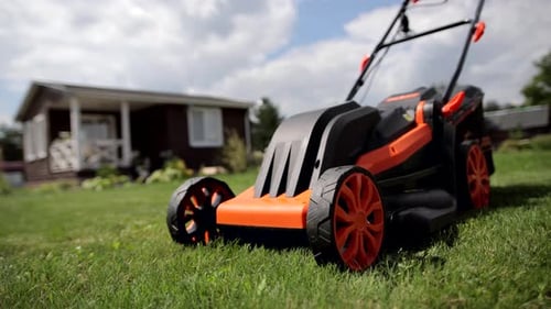 A lawn mower on a lush green lawn on a summer day. Brown house on the background