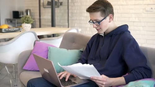 Teenager Using Laptop and Papers on Sofa