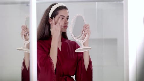 Woman Applying Cream to Face in Bathroom Mirror