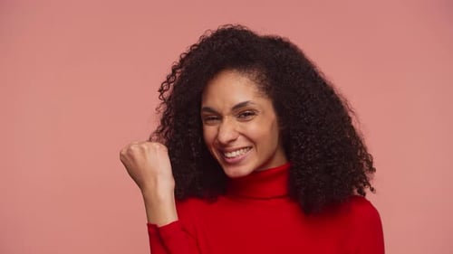 Excited Woman Celebrating Success with Fist Pump on Pink