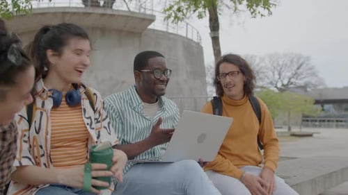 Cheerful College Students Sitting with Laptops in Park and Chatting