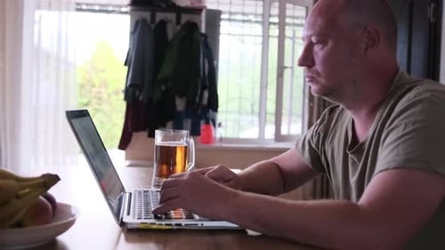 Der Mensch arbeitet an einem sonnigen Tag alleine mit einem Laptop und einem Glas Bier auf dem Tisch zu Hause
