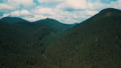 Aerial View of Mountain Range with Lush Forested Slopes Under a Cloudy Sky