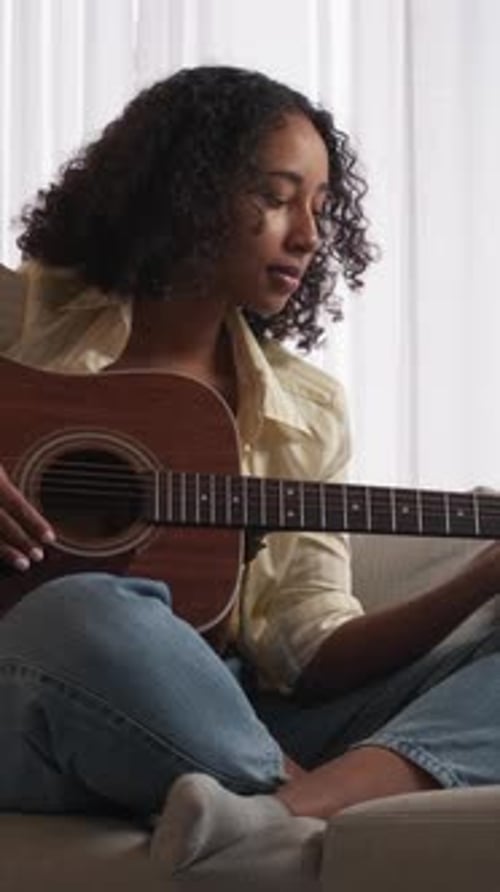 Woman Playing Guitar While Sitting on Couch