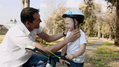 Father teaches son about bicycle safety on a sunny park pathway