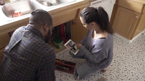 Couple fixing sink plumbing while following online instructions