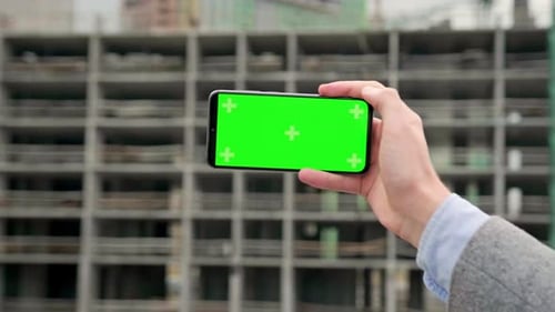 Hand Holding Phone With Green Screen At Construction Site