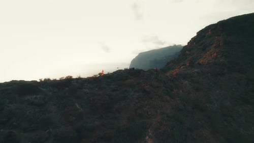 Person running on a rocky cliff with the ocean and mountains in the distance during a misty evening