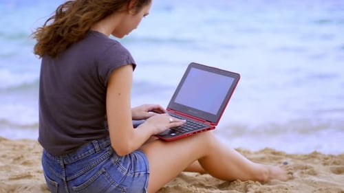 Hübsches Mädchen mit Laptop am Strand. Freiberuflerin, die in der Nähe des Meeres arbeitet. Wunderschön