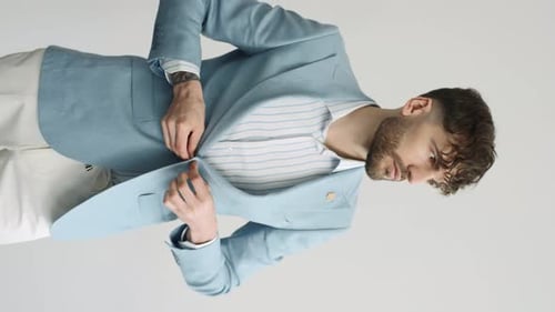Man buttoning his blue jacket on white background in studio