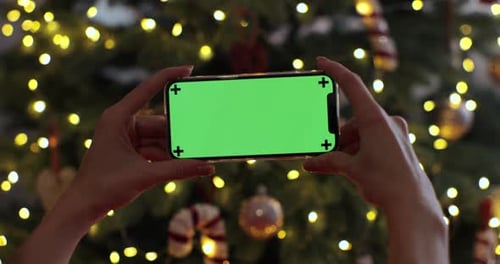 Woman Holding Smartphone with a Green Screen on a Christmas Background